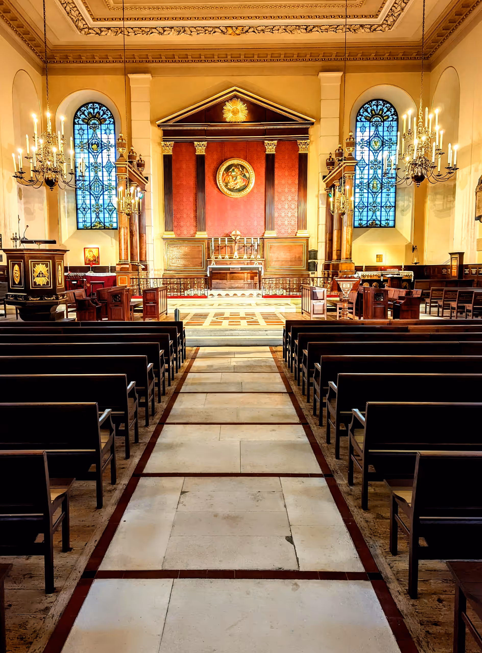 The stone central aisle runs between wooden pews to the altar, flanked by stained-glass windows and chandeliers.