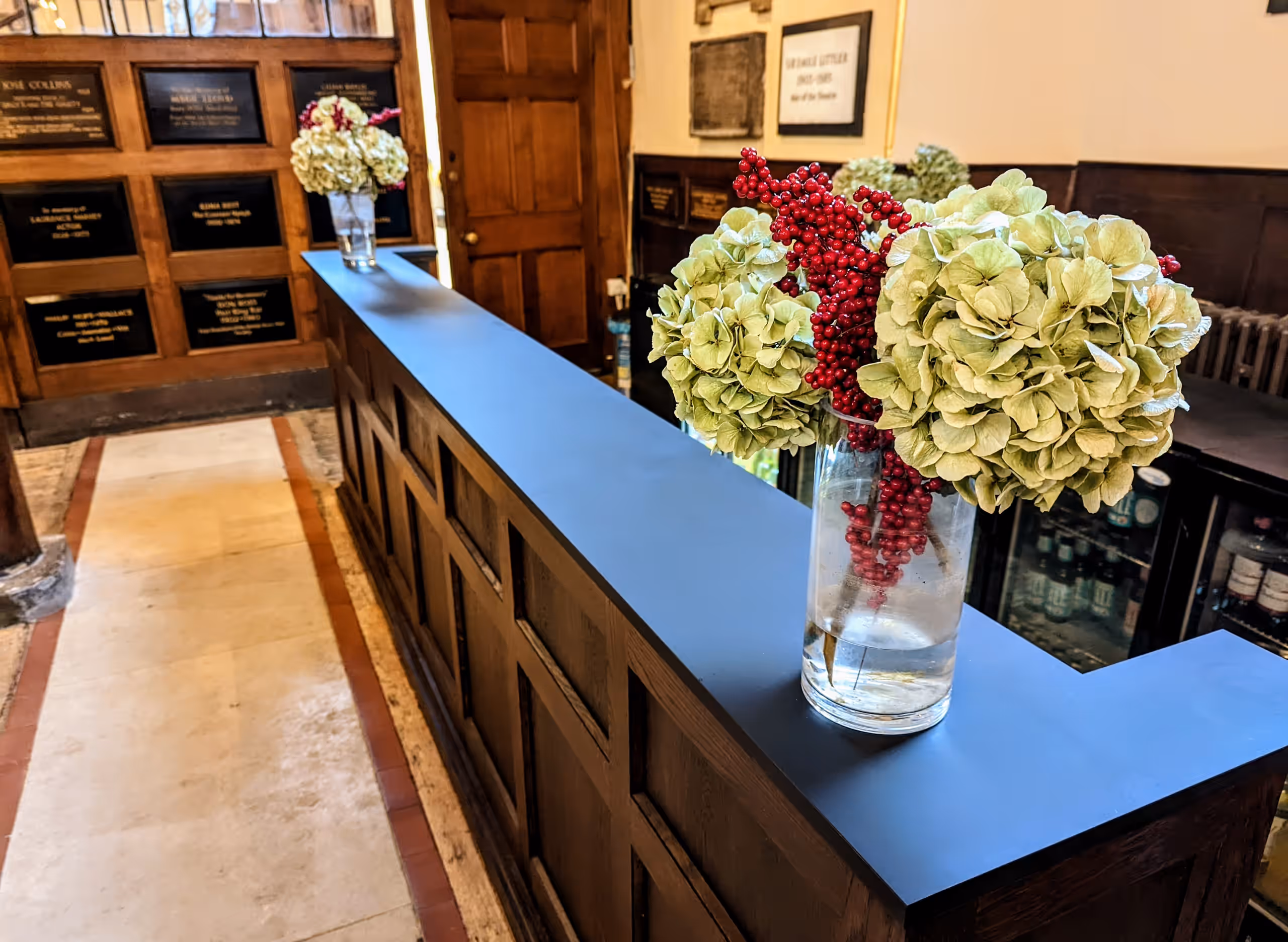 The church bar counter, dressed with hydrangeas and red berries, with memorial plaques on the wall behind.
