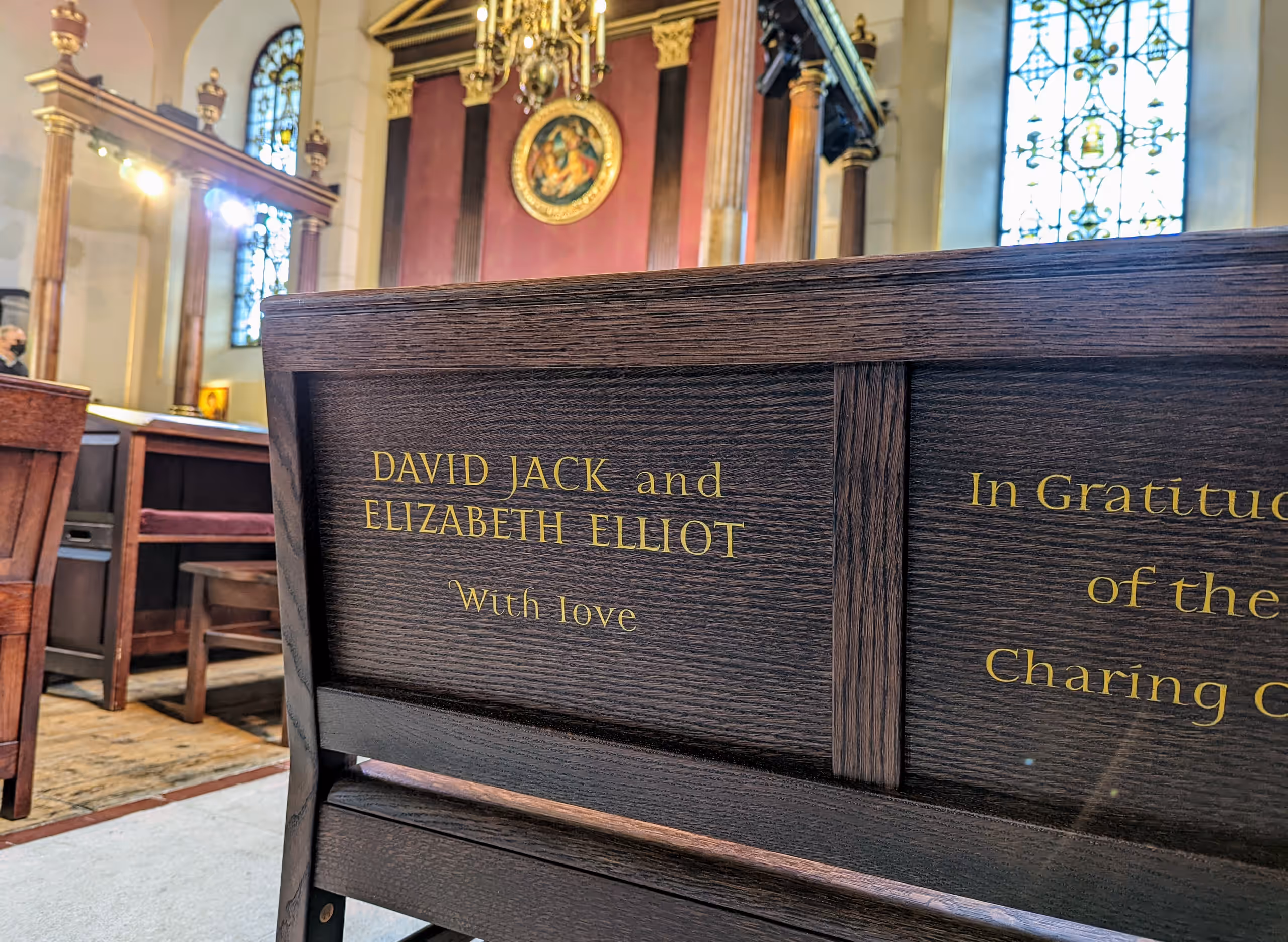 A wooden pew end carved in gold with 'David Jack and Elizabeth Elliot, With love', looking towards the altar.
