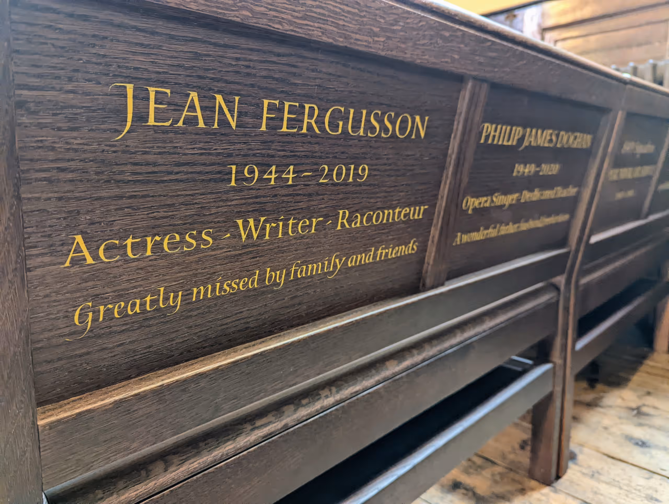 Gilded pew plaques, one reading 'Jean Fergusson 1944–2019, Actress, Writer, Raconteur, greatly missed by family and friends'.