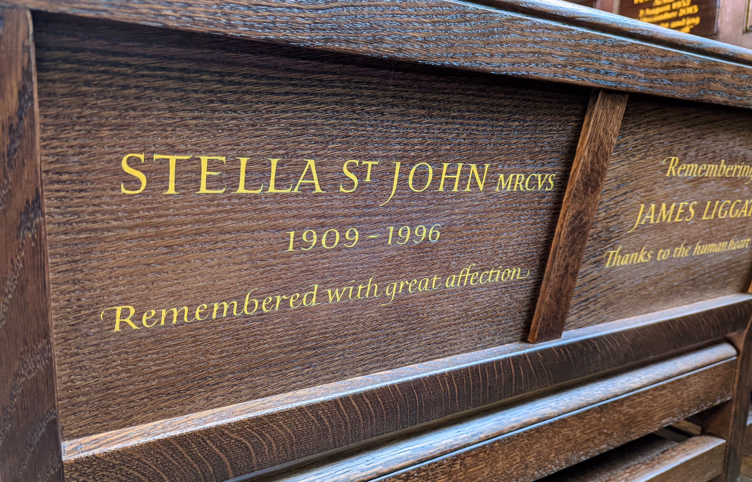 Oak pew inscribed in gold: Stella St John MRCVS, 1909–1996, Remembered with great affection.
