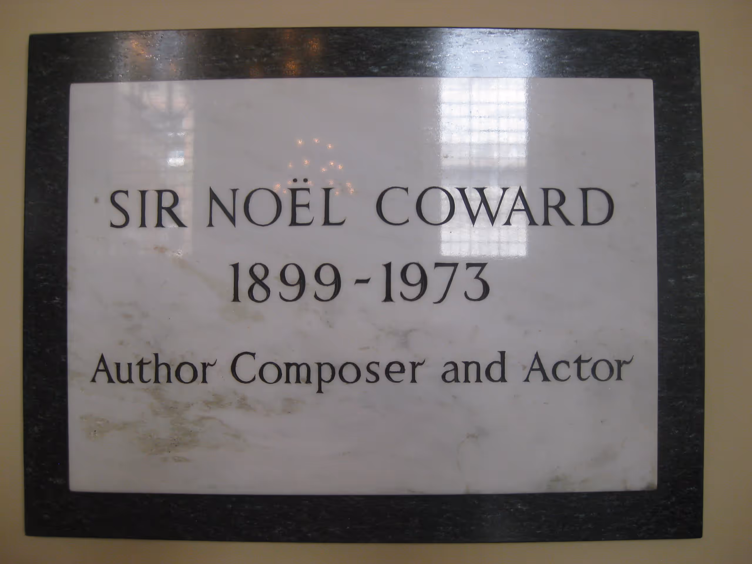 A white marble plaque reading 'Sir Noël Coward, 1899–1973, Author, Composer and Actor'.