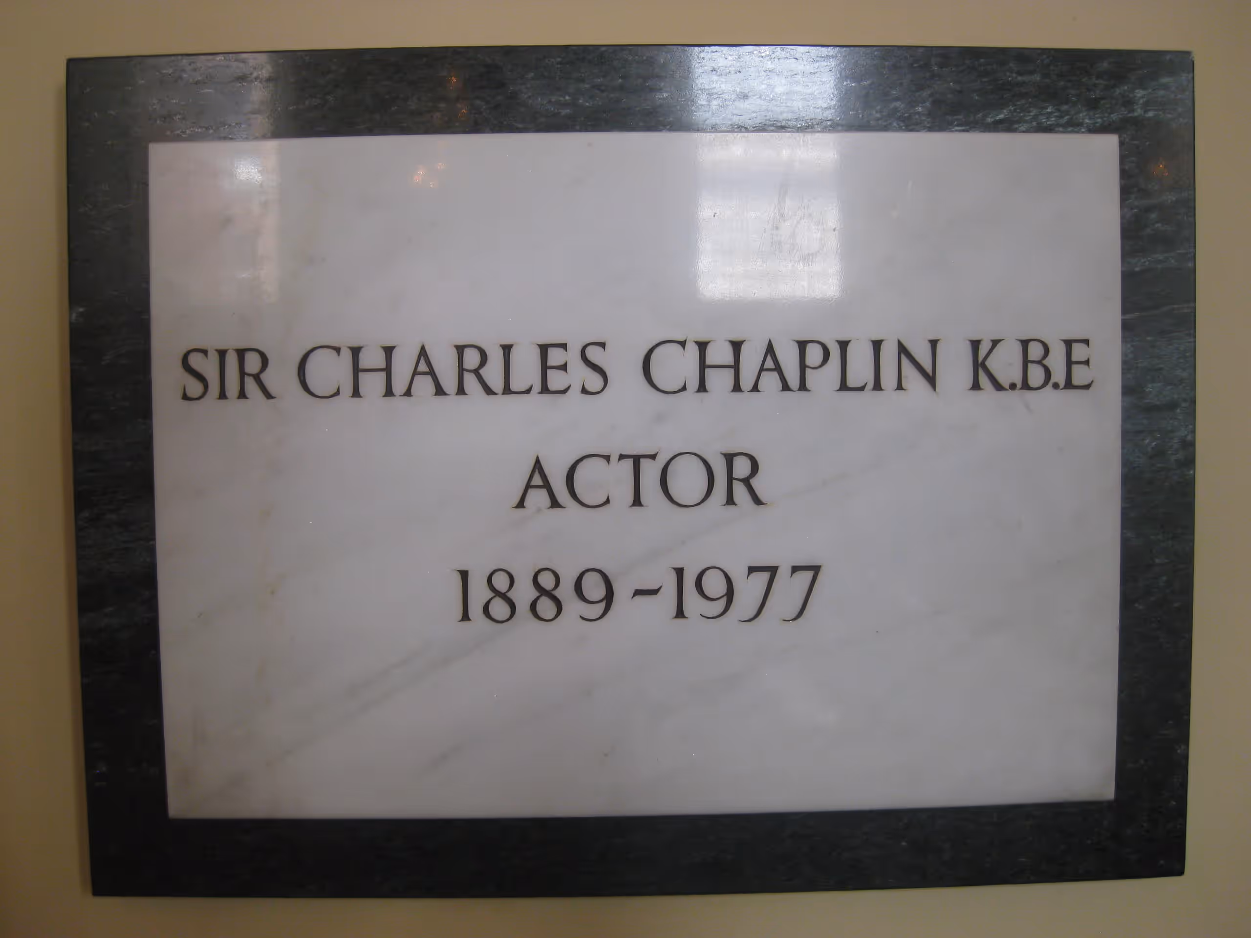 A white marble plaque with a dark border reading 'Sir Charles Chaplin K.B.E., Actor, 1889–1977'.