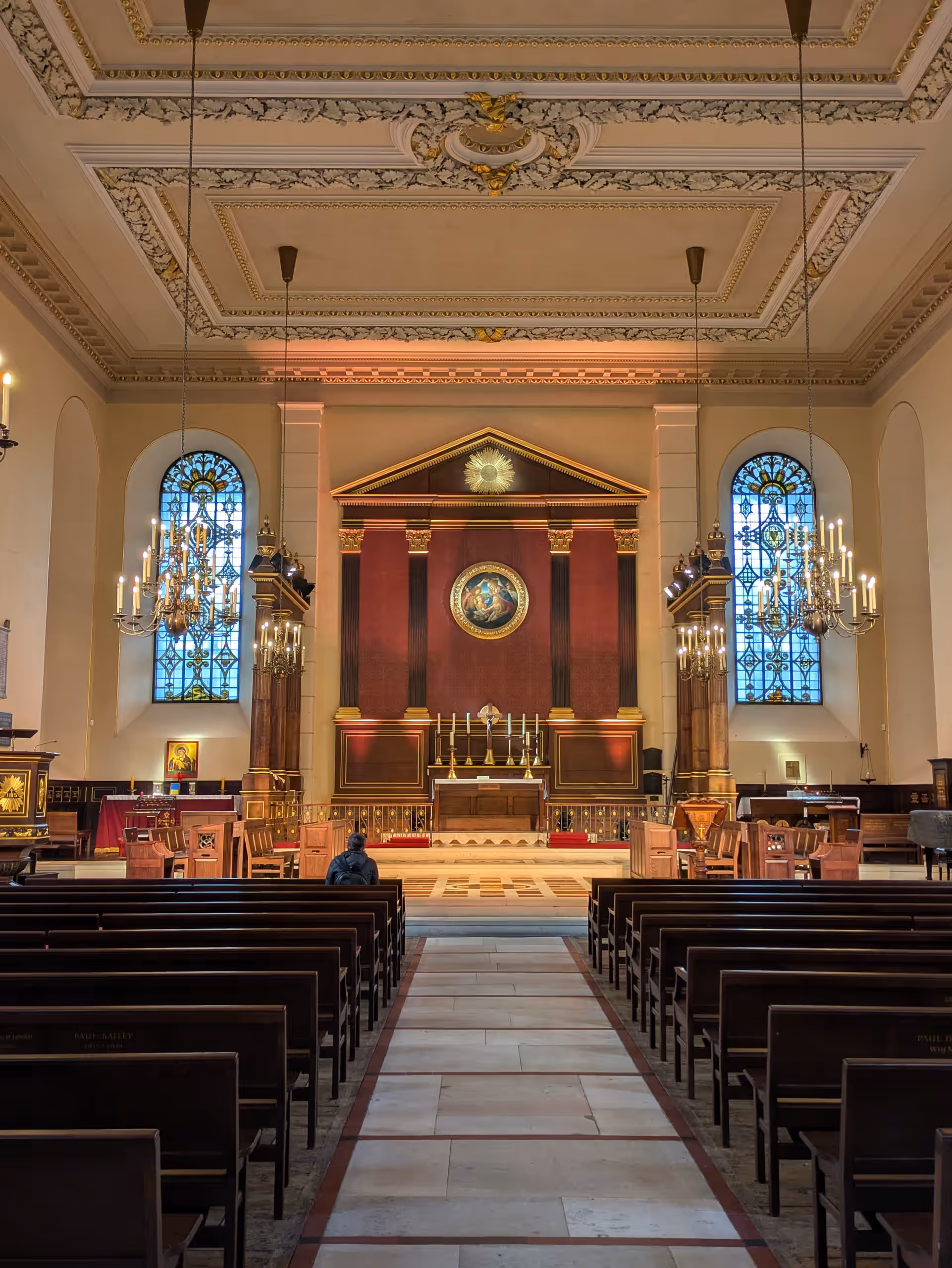 Inside the church, looking down the central aisle between wooden pews to the altar, with chandeliers and stained-glass windows either side.