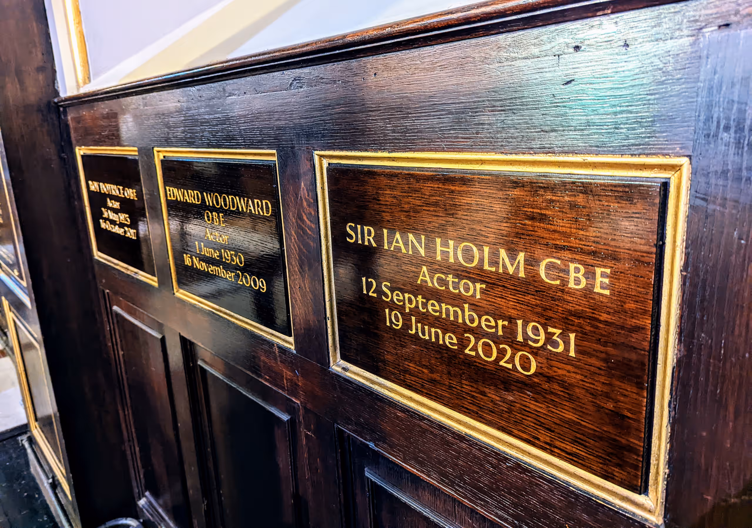 Gilded wooden plaque reading 'Sir Ian Holm CBE, Actor, 12 September 1931 – 19 June 2020', beside plaques to Edward Woodward and others.