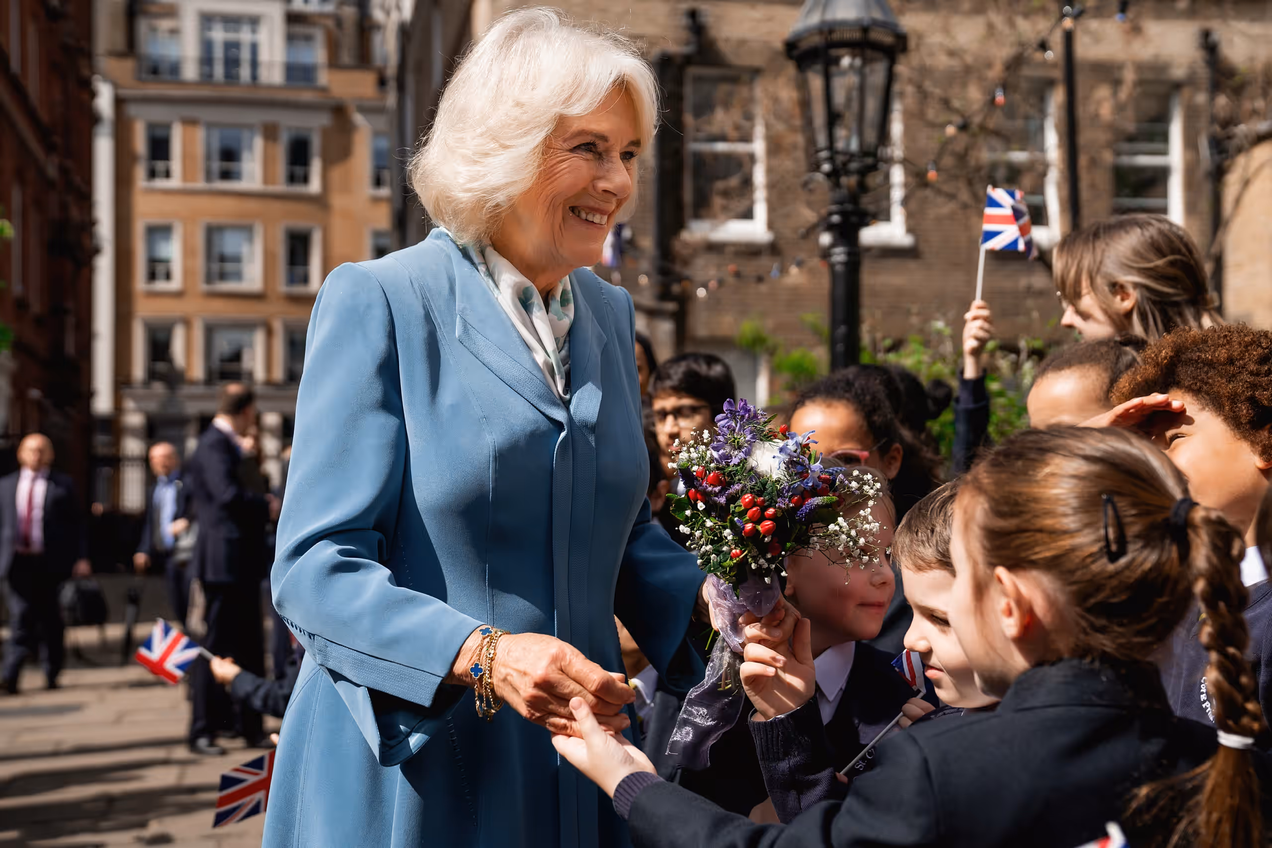 Queen Camilla smiles as schoolchildren waving Union flags present her with a posy of flowers outside the church.